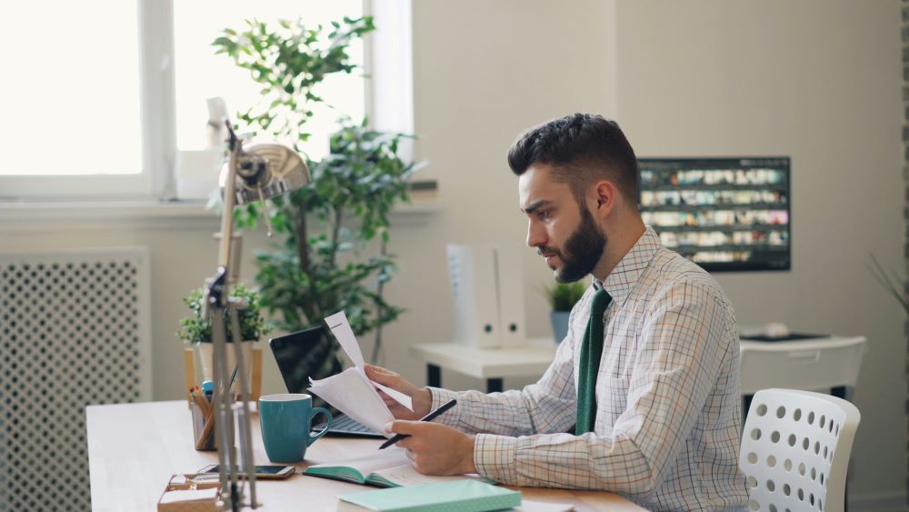 Person at work desk looking at papers with a serious facial expression