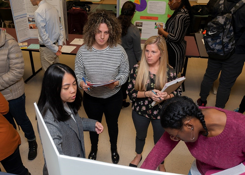 students gather around a poster board to learn about a student project