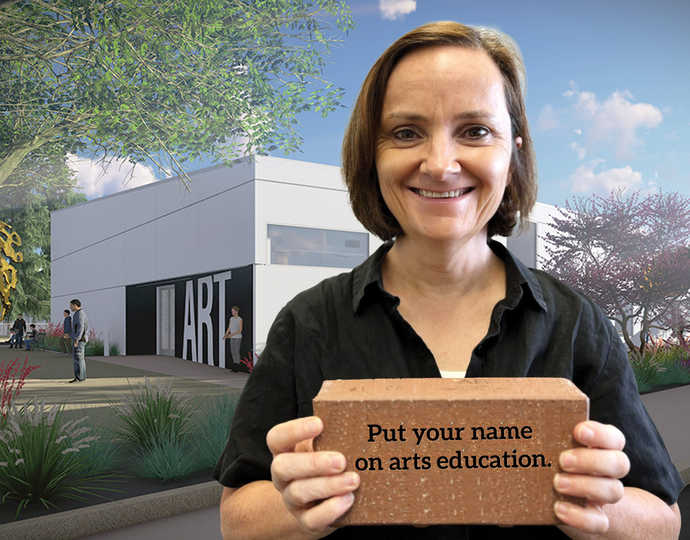 Art Department Chair Rachel Clarke holding brick that reads, "Put your name on arts education"