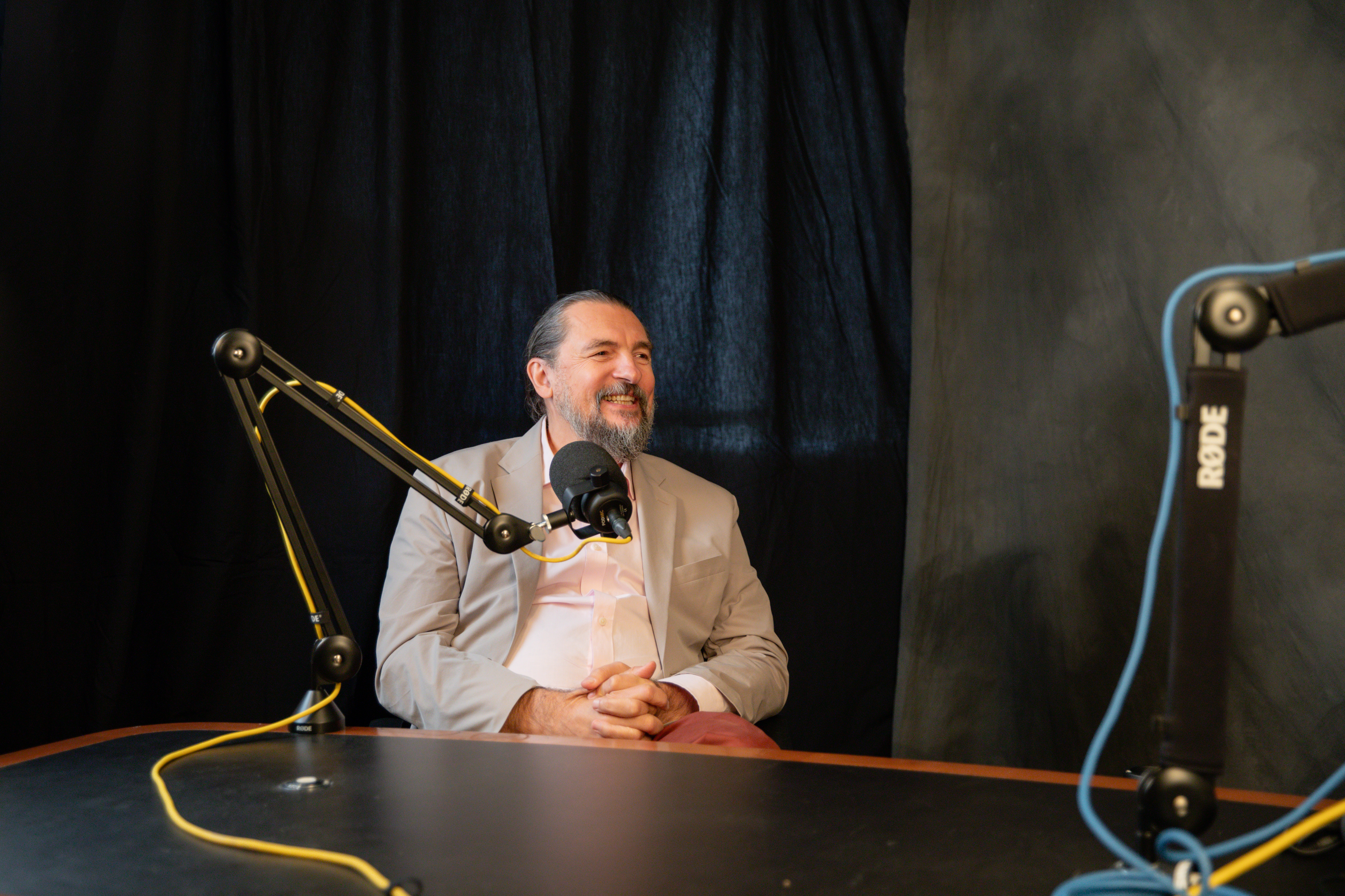 Sasha Sidorkin, sitting at a desk in a studio, smiling with a microphone in front of him