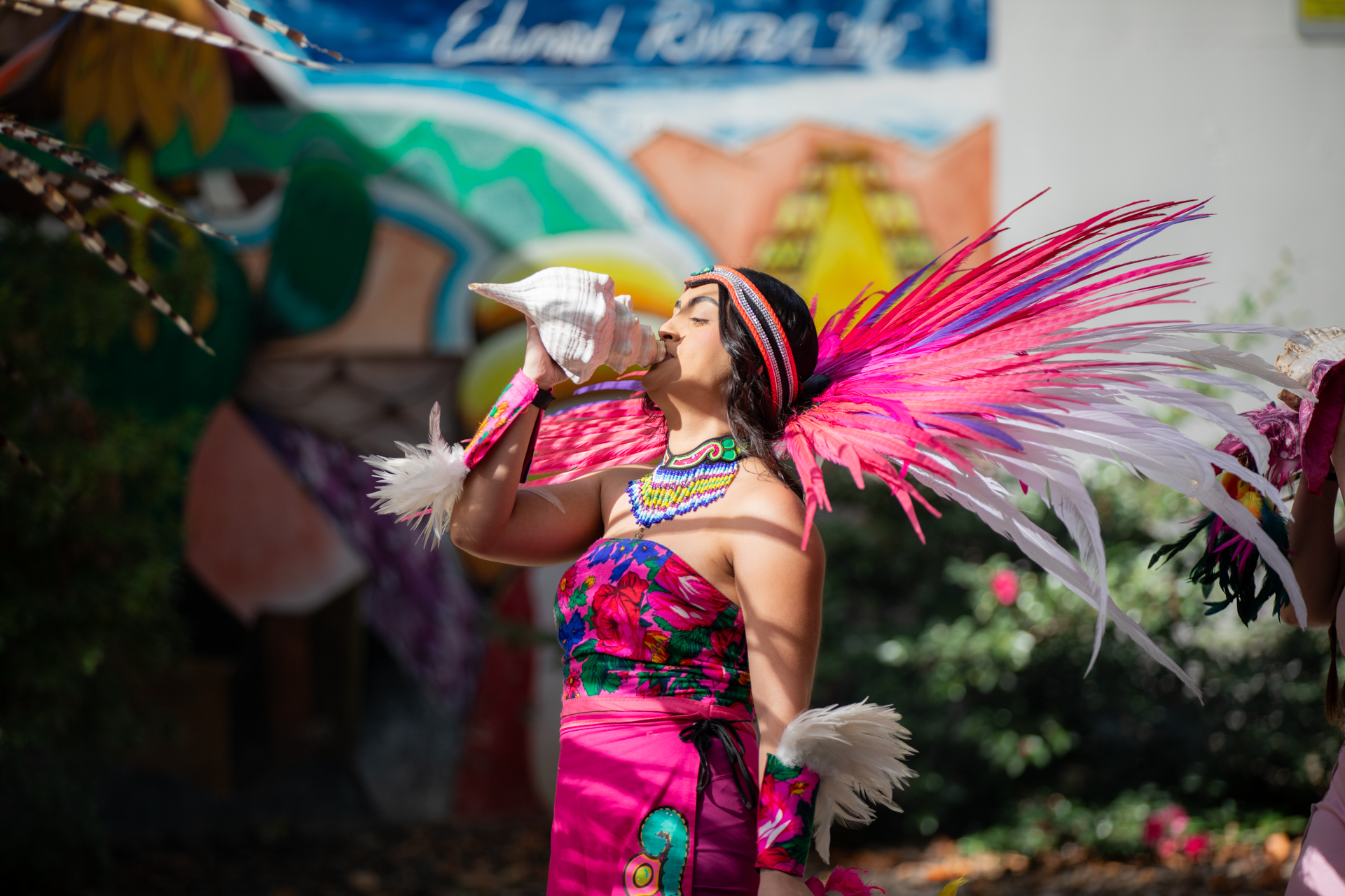 A woman dressed in traditional Mexican clothing blows a conch shell.