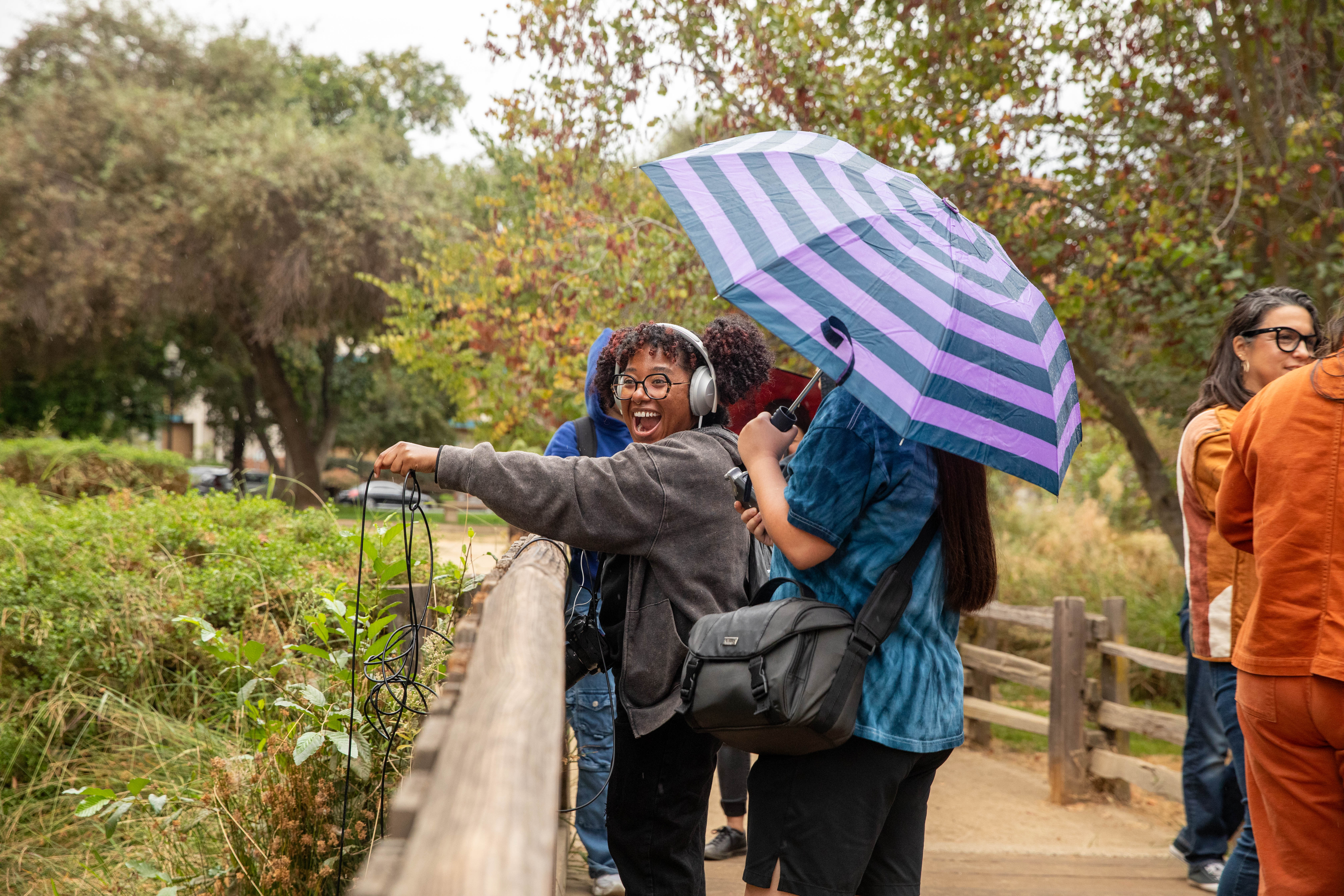 A student wearing headphones drops a listening device off of a bridge into a creek.