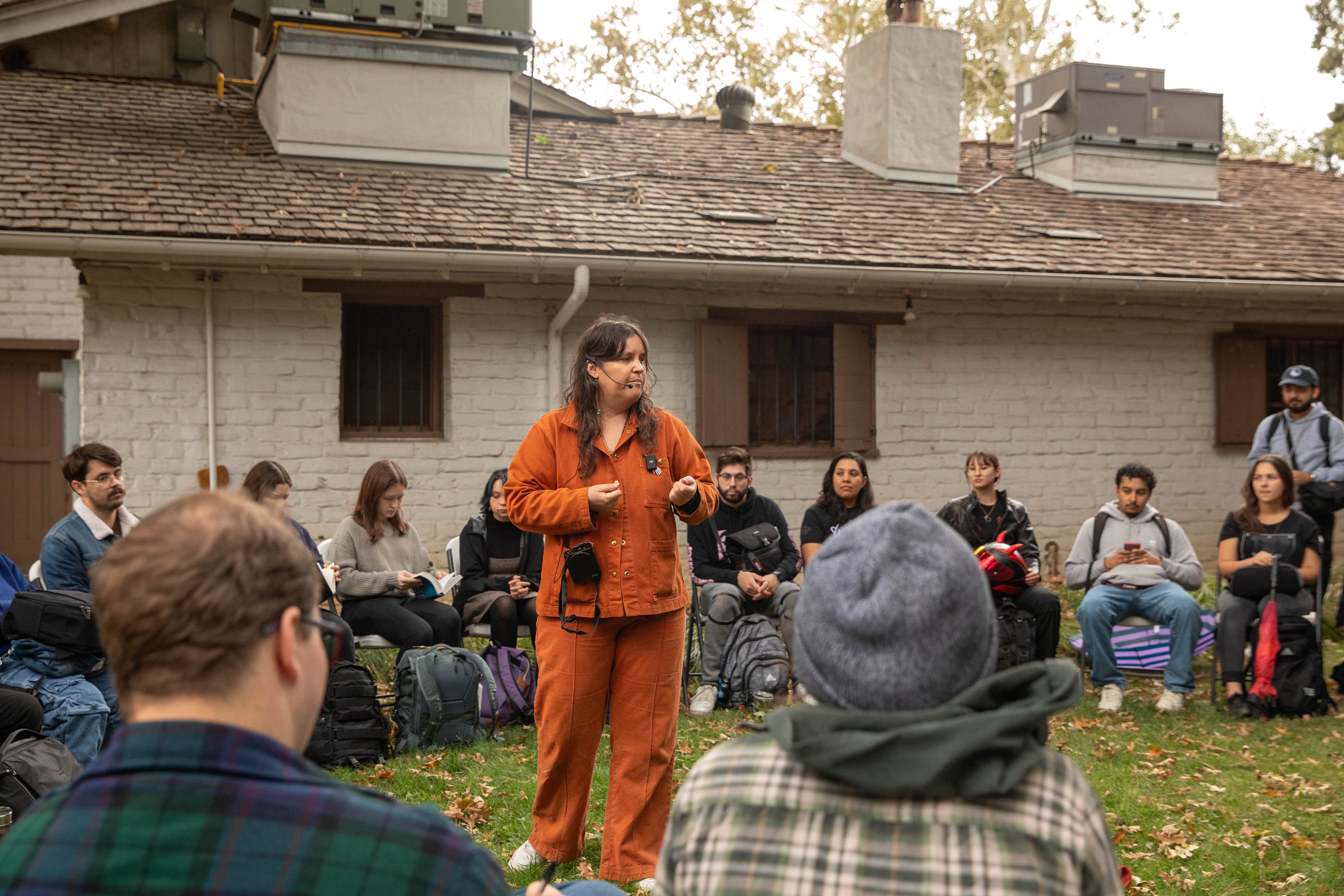 Artist Amy Reed speaking outside to students seated in a circle.