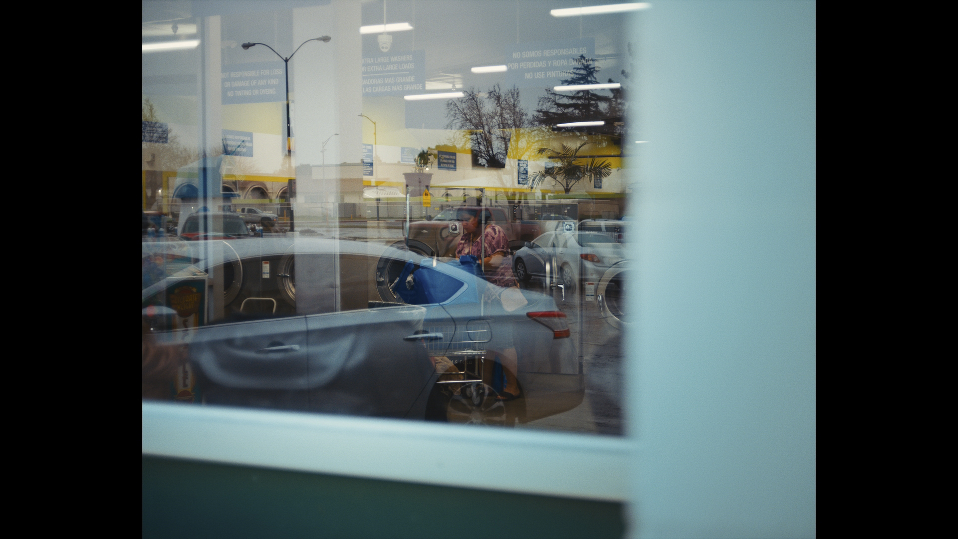 A woman in a laundromat, seen from outside through a window