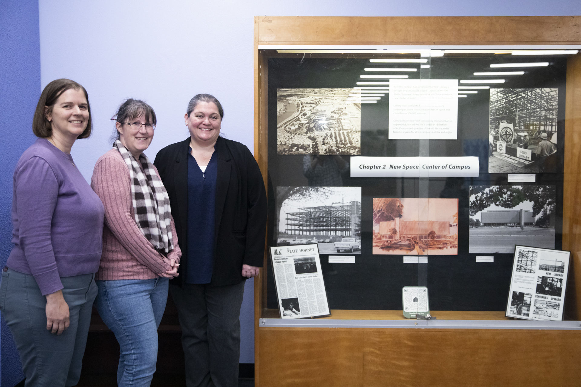 Library staff pose next to one of the showcases highlighting historical University Library items for its 50th anniversary.